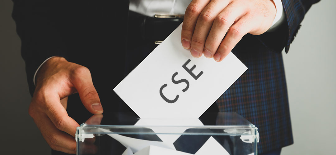 Mains glissant un bulletin portant l'inscription CSE dans une urne transparente, illustrant le processus d'élections du Comité Social et Économique